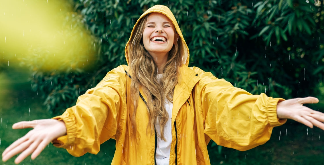 Woman in yellow rain jacket outside with her arms outstretched as she laughs