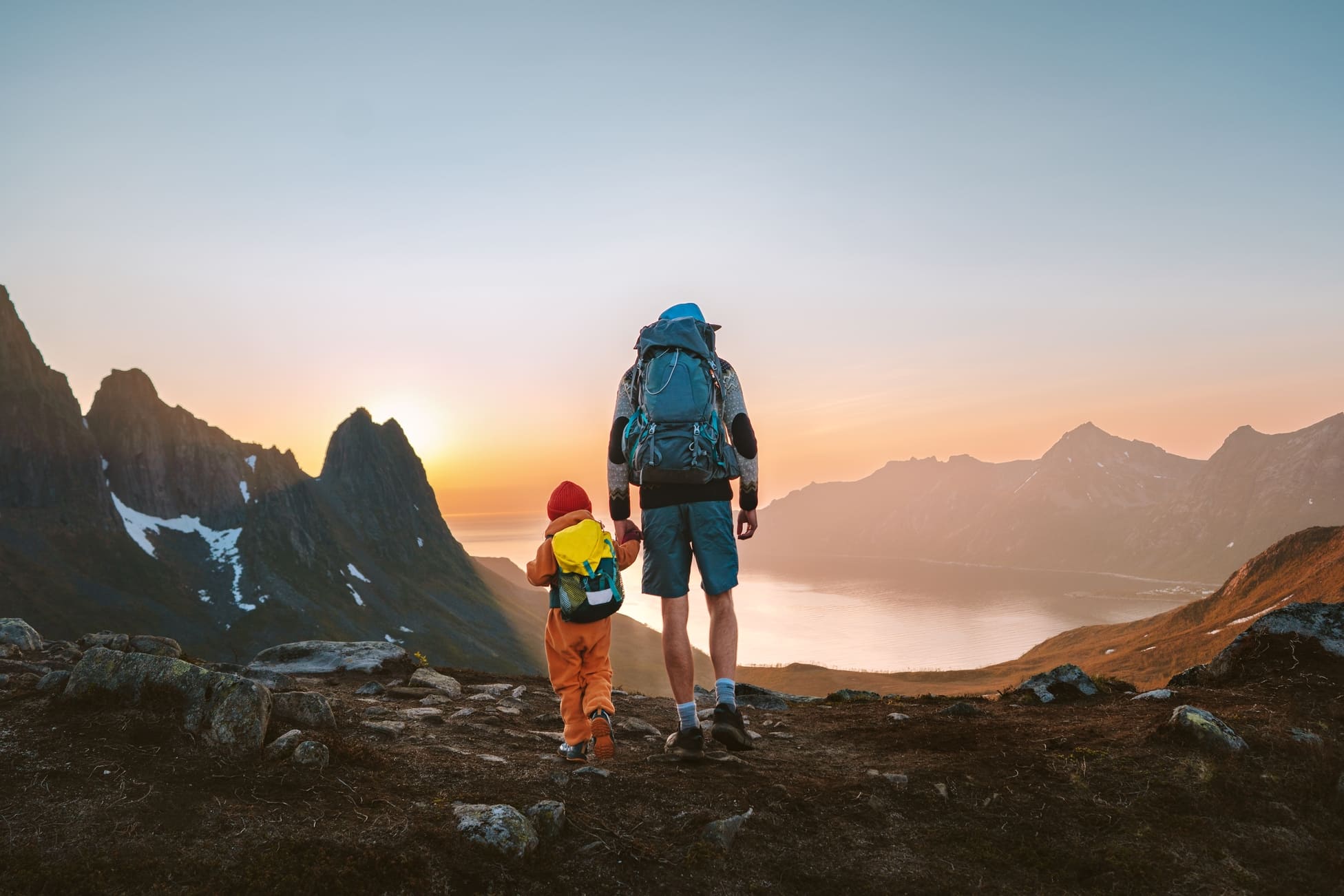 Man hikining in the mountains holding hands with his child in climbing gear