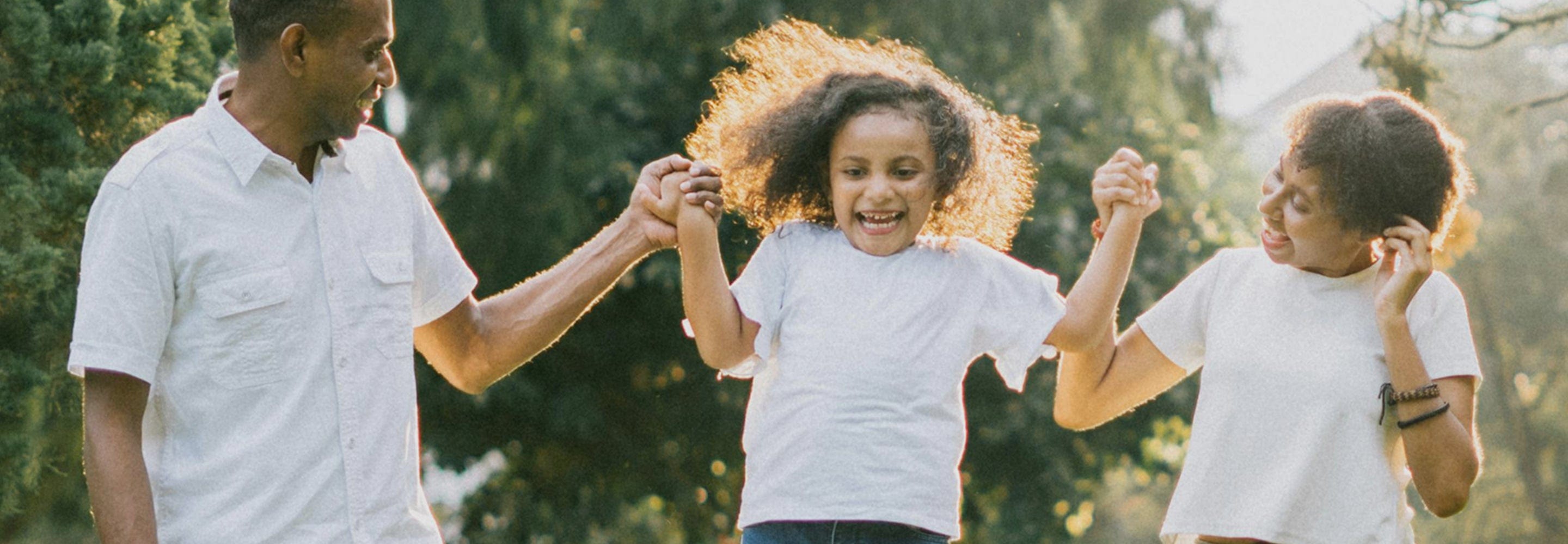 A family, father, mother and daughter skipping in the sun in nature