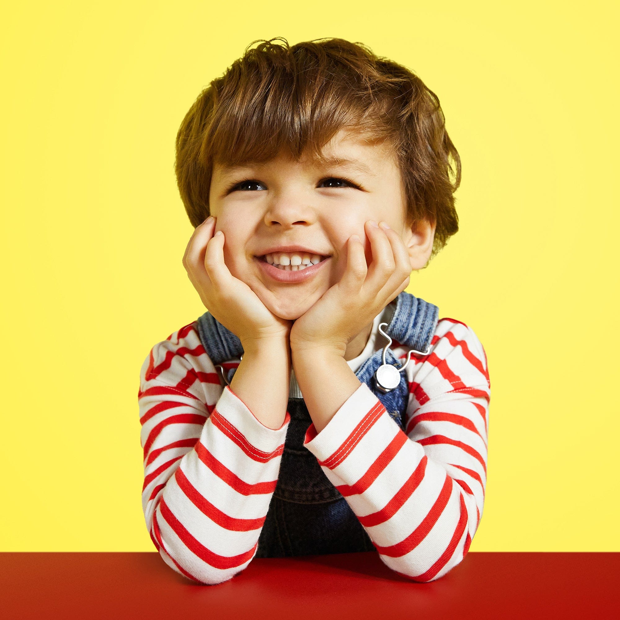 Young boy with brunette hair smiling and leaning his face in his hands