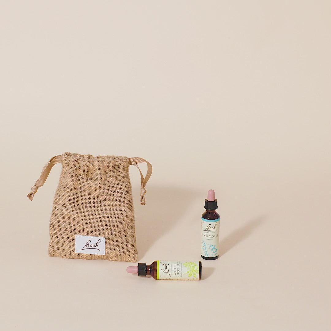 A hand taking out the Bach™ Original Flower Remedy Crab Apple dropper from the burlap bag and placing it next to the Bach™ Original Flower Remedy Rock Water dropper and Bach™ Original Flower Remedy White Chestnut dropper which is lying down.