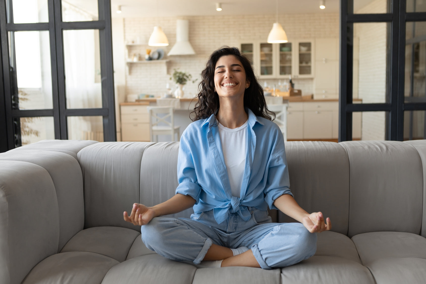 Woman grinning with her legs crossed, sitting on the couch and meditating
