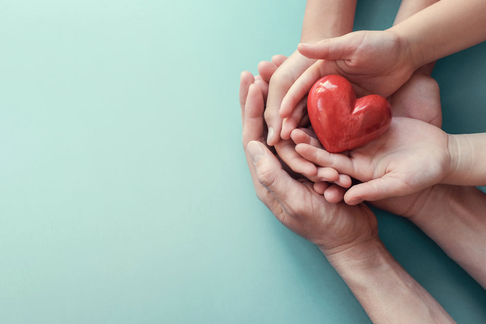 A families hands stacked on top of one another holding a red love heart