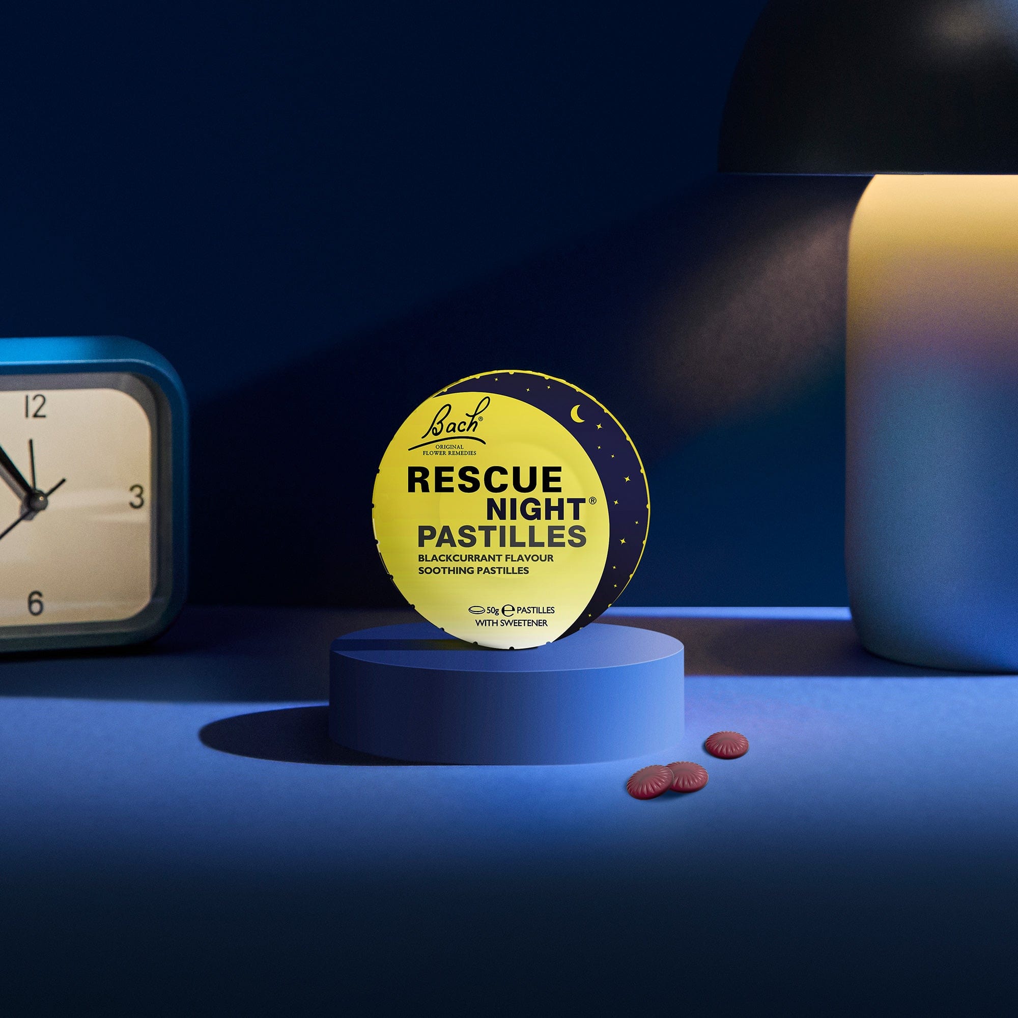 Rescue Night® blackcurrant pastilles for sleep on a bedside table next to a lamp and alarm clock